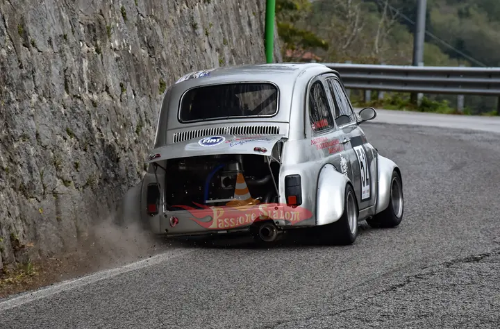 Fiat 500 numero 52 con il motore a vista e l'adesivo Passione Slalom sul portellone, che sfiora il muretto di pietra in uscita di curva.