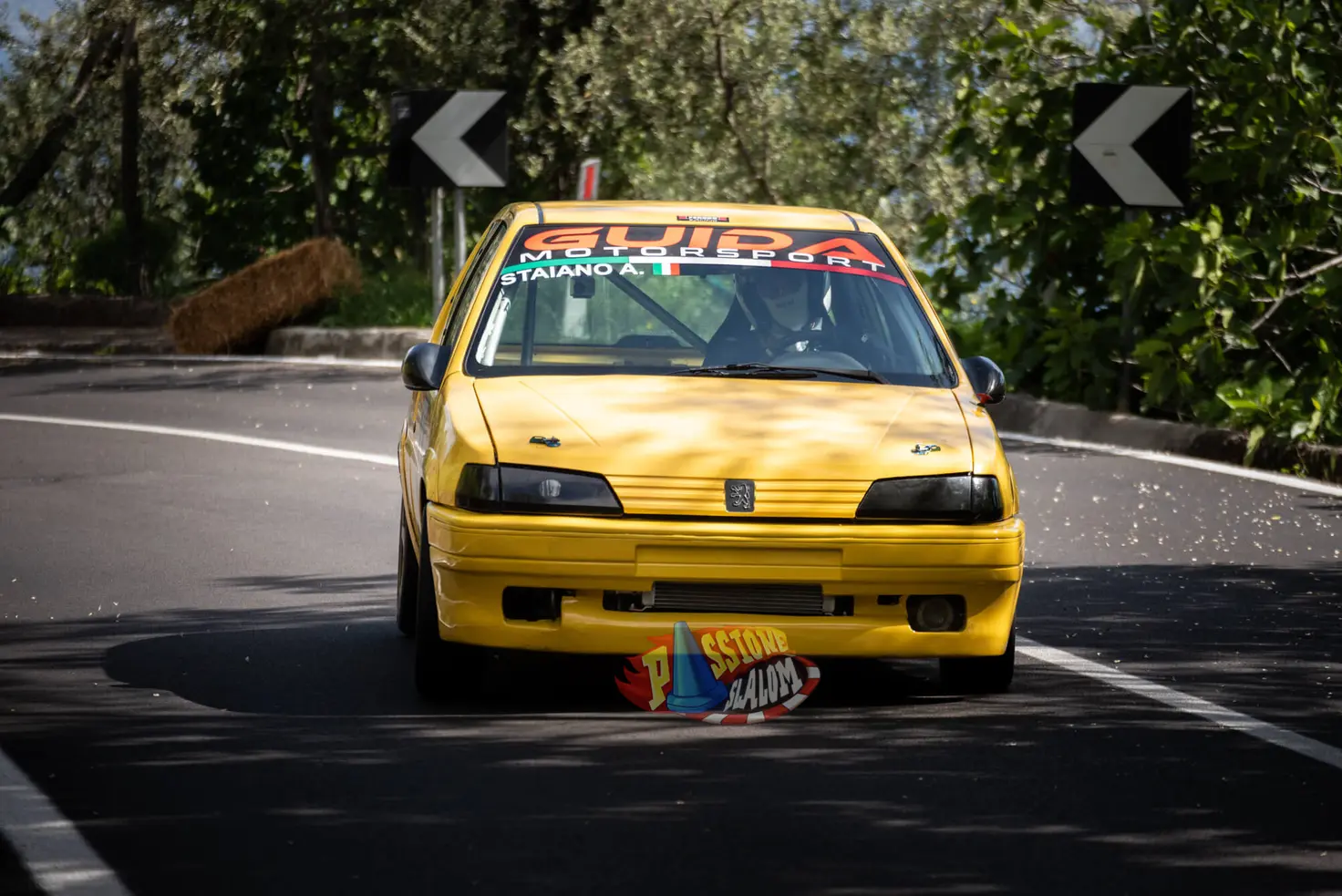 Peugeot 106 gialla di Guida Motorsport in uscita di curva, tra le frecce direzionali e la balla di fieno a bordo strada.