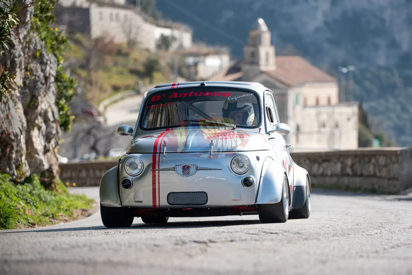 Fiat 500 elaborata di D'Antuono Engineering in salita su una strada di costiera, con il campanile del paese sullo sfondo.